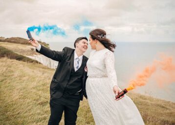Two newlyweds on the White Cliffs of Dover with blue and orange smoke grenades