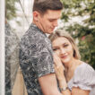 A girl resting her head on her partner's chest as he leans against the side of a glass house