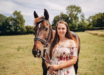 A girl in a floral dress standing with a brown horse