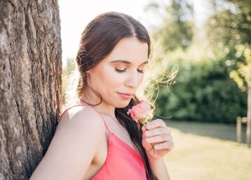 Girl leaning against a tree in a park holding a flower