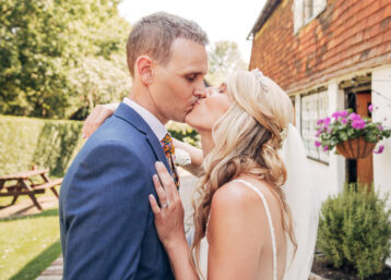 A wedding couple sharing a romantic kiss outside a rustic countryside pub