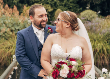 A wedding couple smiling and embracing on a bridge over a stream