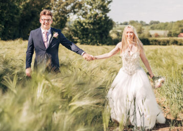 A wedding couple holding hands and smiling amongst a field of green wheat