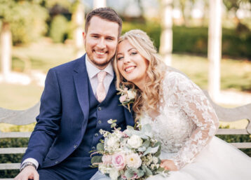 A wedding couple sat on a bench together smiling