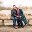 Expectant couple sat on a bench in front of a lake in Richmond Park