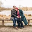 Expectant couple sat on a bench in front of a lake in Richmond Park
