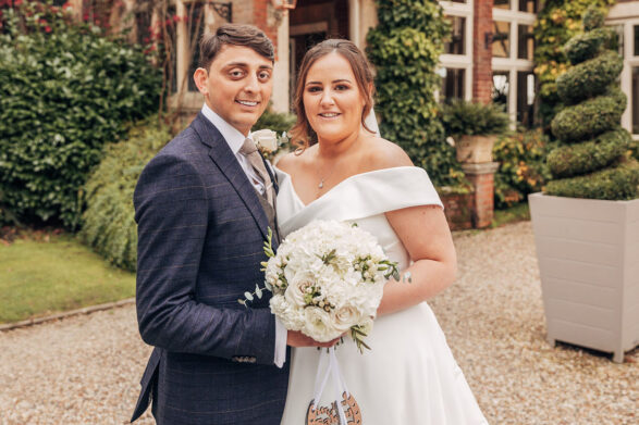 A wedding couple smiling outside in front of a country hotel