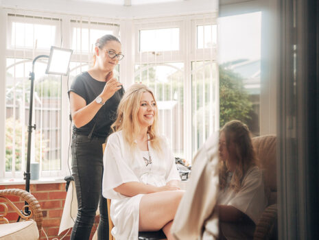 A bride smiling as she has her hair and makeup done on the morning of her wedding