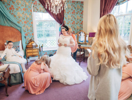 A bride getting into her wedding dress surrounded by her bridesmaids