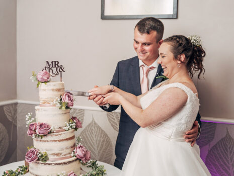 A wedding couple smiling as they cut their wedding cake