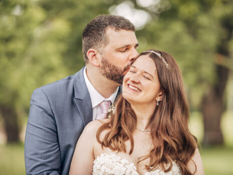 A wedding couple smiling and embracing outdoors amongst the trees
