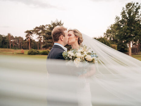 A wedding couple kissing at sunset as the bride's veil flicks in the wind