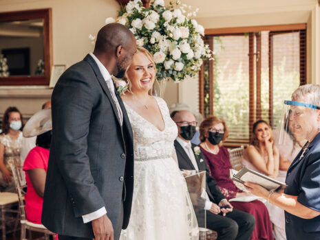 A wedding couple smiling as their guests look on during their wedding ceremony