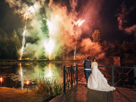 A wedding couple stood overlooking a lake watching a firework display