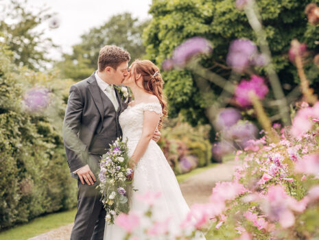 A wedding couple sharing a kiss amongst flowers and gardens at Wadhurst Castle